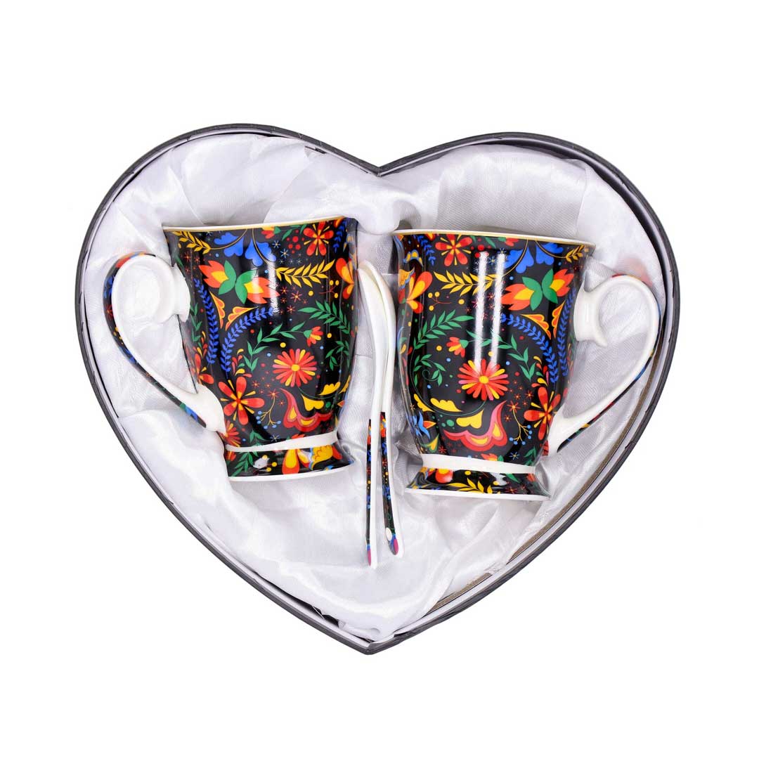 Two colorful floral mugs with matching spoons in a white tissue-lined heart-shaped gift box, a bright gift set for tea lovers