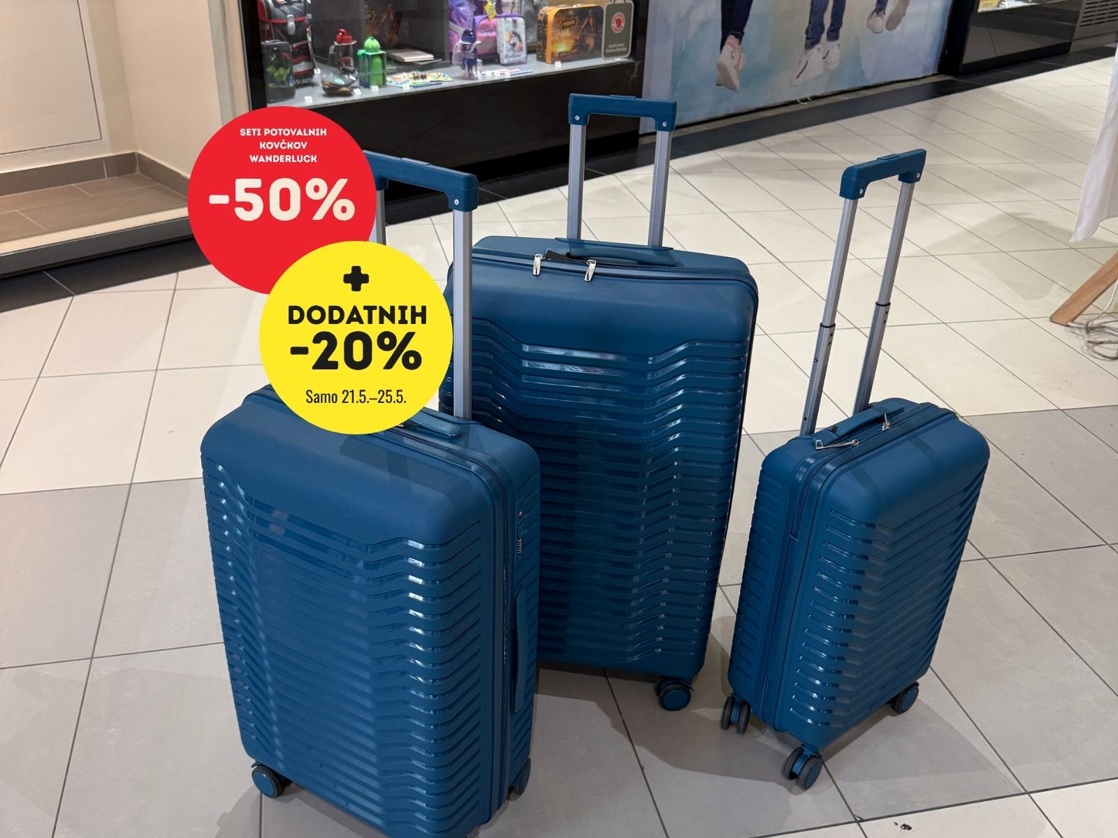Blue hardside luggage set with rolling wheels and handles in a shopping mall, featuring red and yellow sale circles showing discounts. -50% and -20%.