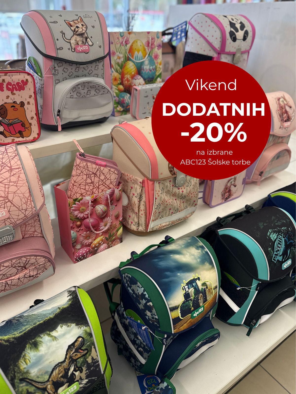 Assorted kids' backpacks on display with a large red circle advertising 'Vikend DODATNIH -20% na izbrene ABC123 Šolske torbe'