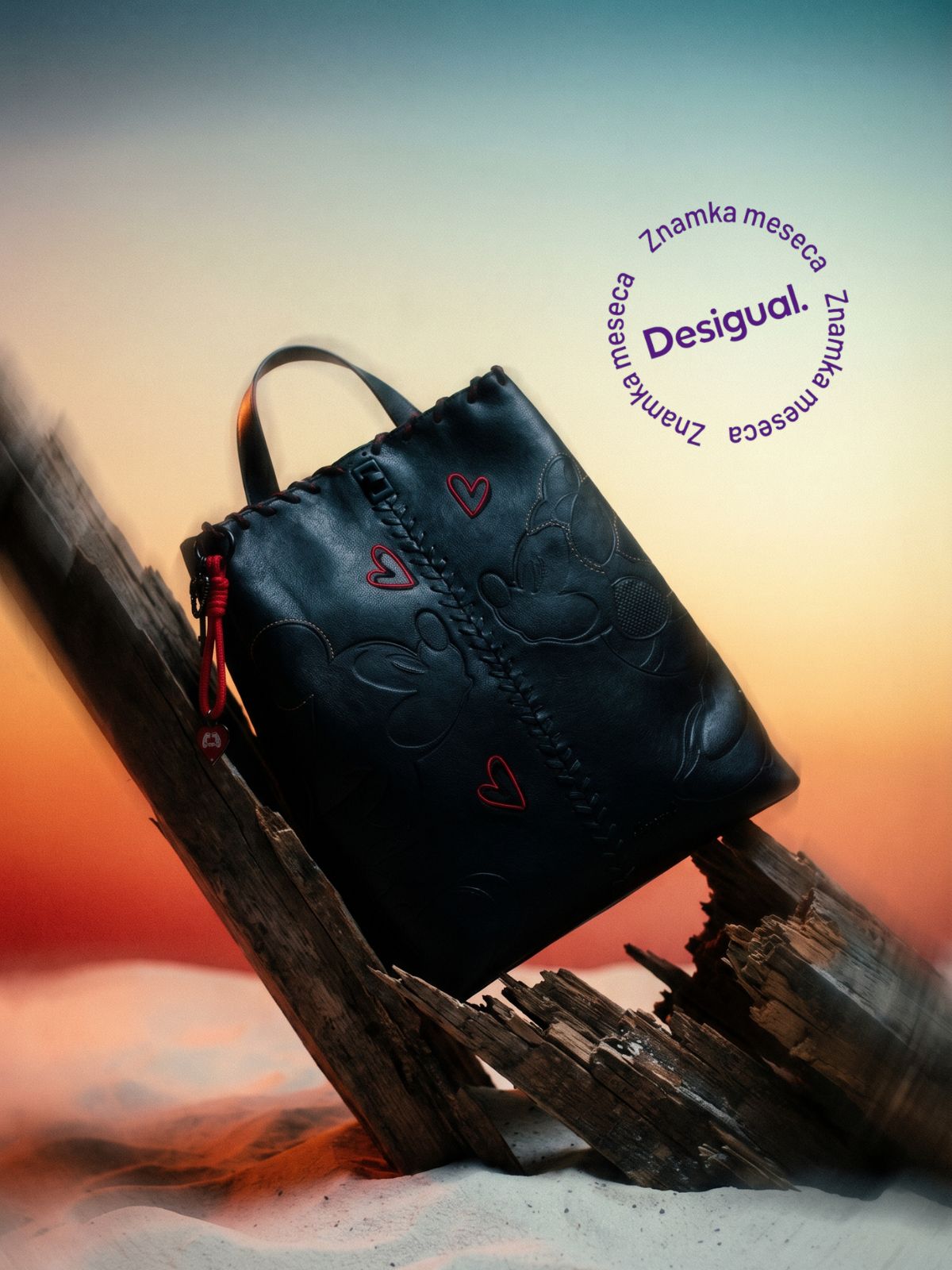 Black leather handbag with red heart embroidery resting on a weathered wooden beam at sunset