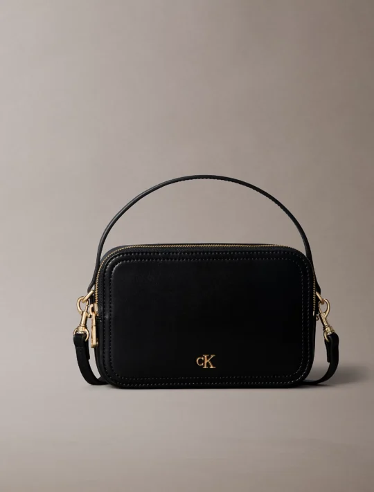 Black leather handbag with gold hardware and a top zipper, visible CK logo on the front.