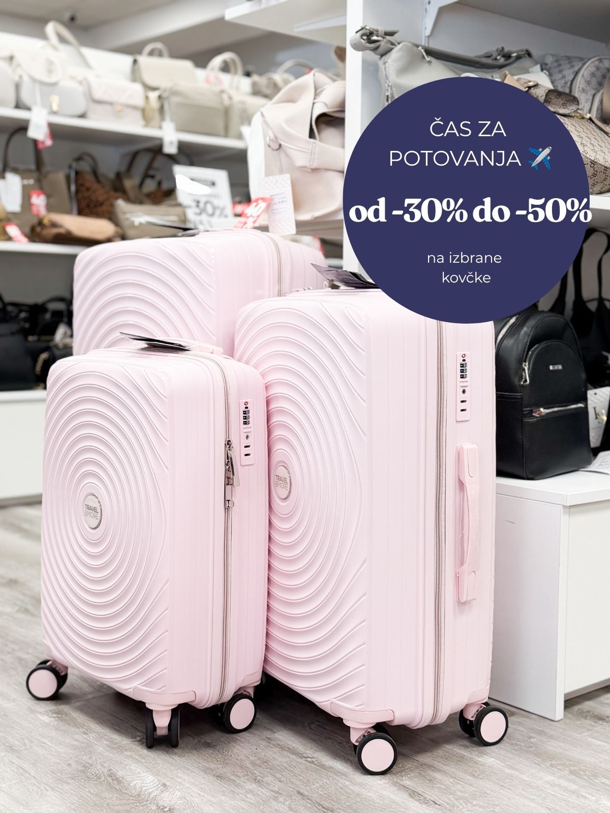 Two pink hard-shell suitcases in a shop with a large blue promo circle advertising travel discounts (30–50%).